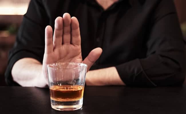 Person refusing a glass of alcohol, hand gesture signaling no. (AI-generated)