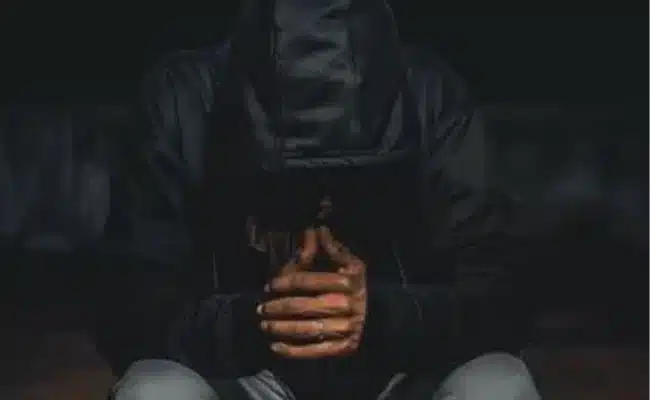 Person in dark hoodie clasping hands, contemplative mood. (AI-generated)