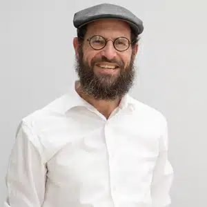 Man in glasses and cap smiling, wearing white shirt against plain background. (AI-generated)