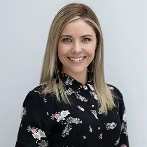 Smiling woman with blonde hair in a floral blouse, posing against a plain background. (AI-generated)