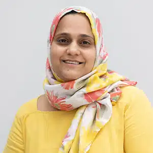 Smiling woman in a colorful hijab and yellow top against a gray background. (AI-generated)