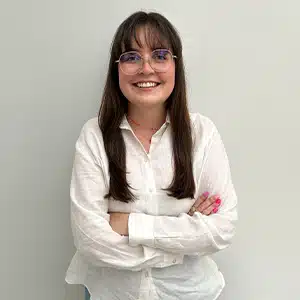 Smiling woman in glasses and white shirt, arms crossed, stands confidently. (AI-generated)