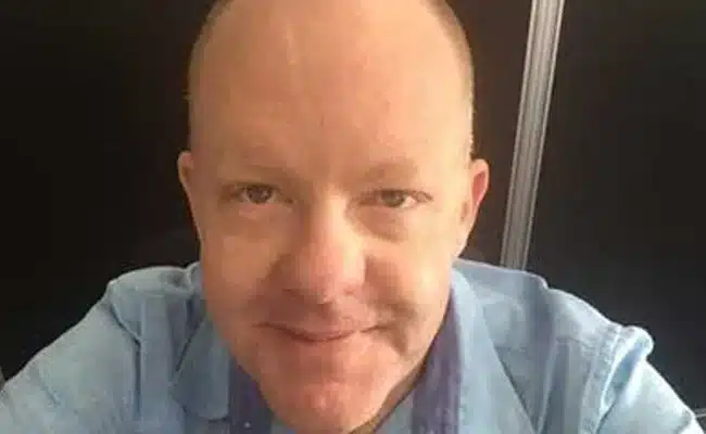 Smiling man in blue shirt, close-up, black background. (AI-generated)