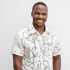 Smiling man wearing a white floral shirt against a plain background. (AI-generated)