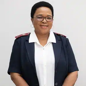Nurse in uniform smiling, wearing glasses, standing against a neutral background. (AI-generated)