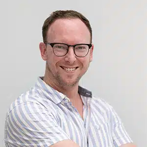 Smiling man with glasses in a striped shirt, folded arms. (AI-generated)