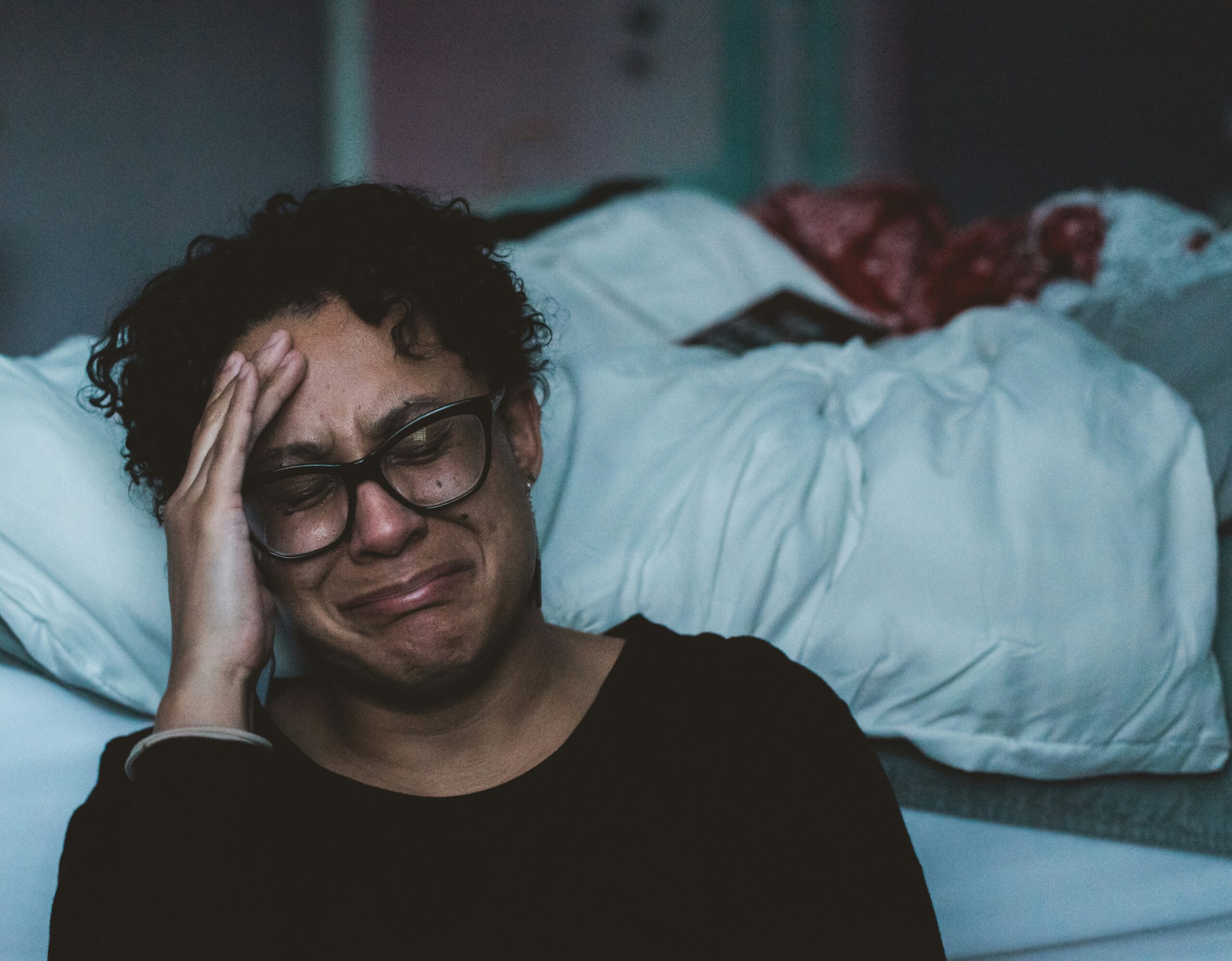 Person having an emotional moment, sitting by a bed in dim lighting. (AI-generated)